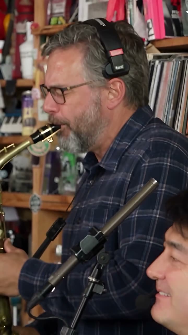 Frame at 13 seconds from the Vellm example video made from test photos: the sax player in a navy plaid shirt and headphones, the keyboard lead in the foreground.